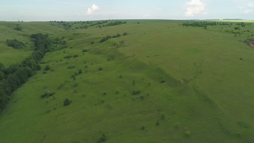 Large, open field with a river running through it. The grass is lush and green, and the sky is clear and blue. Evening summer natural landscapes of the Nizhny Novgorod region Russia