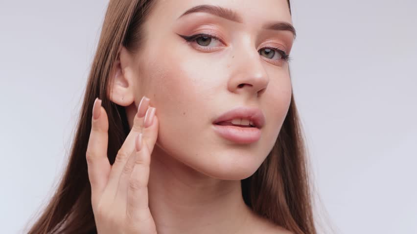 Portrait of an attractive girl with healthy clear skin and beautiful makeup, she applies moisturizing serum. The girl shows her well-groomed skin on her face and neck.