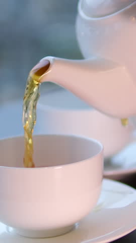 Top down shot of pouring milk into a beautiful floral patterned tea cup with tea in it. Close up