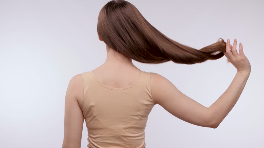Young beautiful girl in a beige sweater with long hair. The girl combs her hair.