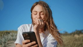 Smiling woman reading smartphone sms at grassy hill closeup. Joyful windy hair lady messaging online watching social media at shore. Attractive girl browsing mobile phone. Digital lifestyle concept  - Powered by Shutterstock - Get 15% off with code: PIKWIZARD15