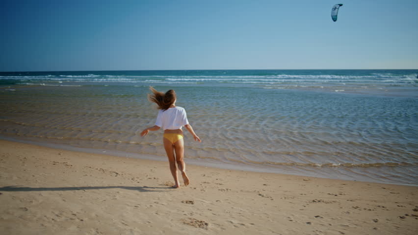 Carefree girl running beach rear view. Happy sexy woman enjoying peaceful sand coastline in yellow bikini. Joyful tourist lady relaxing at calm sea waves rejoicing vacation. Feeling good concept 