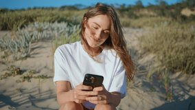 Closeup lady holding smartphone at sunny sandy hills. Smiling woman browsing cell online messaging at beach. Attractive relaxed girl reading sms texting friend. Social networking communication concept - Powered by Shutterstock - Get 15% off with code: PIKWIZARD15