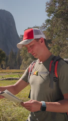 A male hiker actively explores the stunning and breathtaking landscapes of Yosemite National Park, equipped with a detailed map in hand, fully immersed in the surrounding beautiful nature