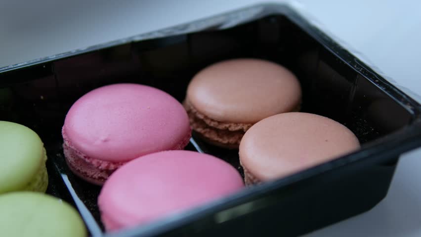 plate with macaron cookies in a variety of spring colors stacked, pink background. Hand reaches in and removes top cookie.