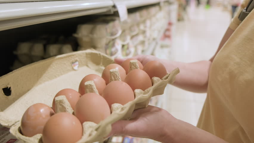 Woman inspects chicken eggs in box in supermarket before buying