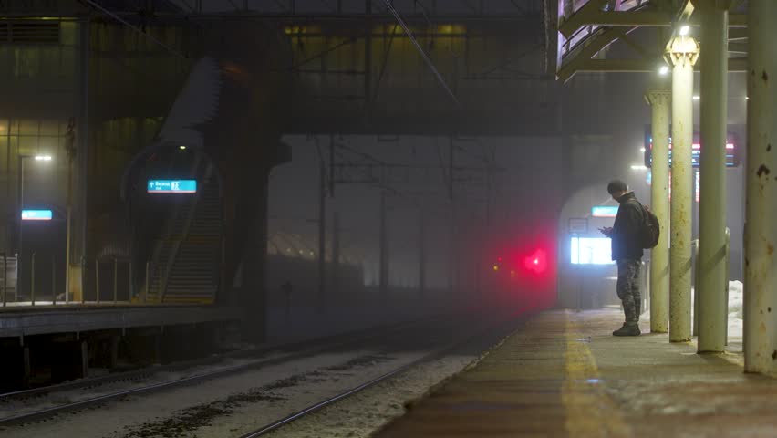 Cold winter night on rail station, person wait on platform under fog, looking for delayed train. No sign of arrival, last train already gone, silence and darkness, wait for next electric train arrival