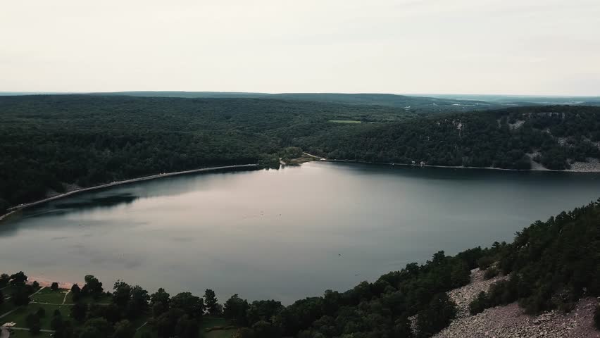 A breathtaking aerial view of Devils Lake in Wisconsin, showcasing its tranquil waters, lush green forests, and surrounding cliffs.