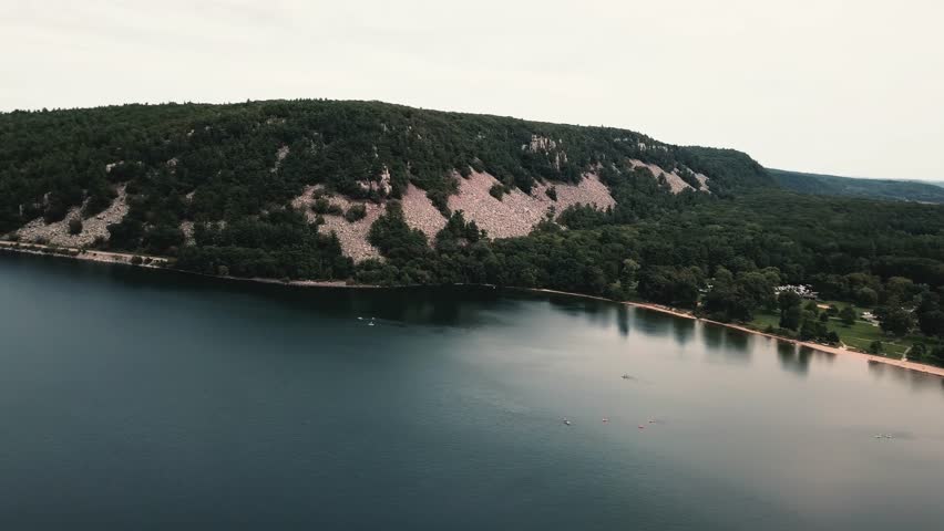 Drone view of Devils Lake in Wisconsin featuring a tree-lined shoreline, clear water, and steep rocky bluffs.