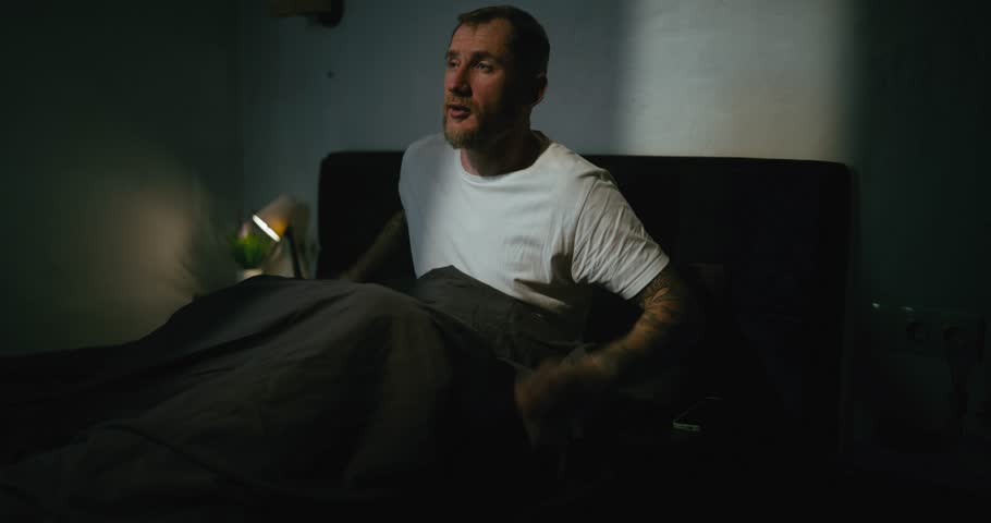 A guy in a white T-shirt wipes his face after waking up in his black bed in the morning