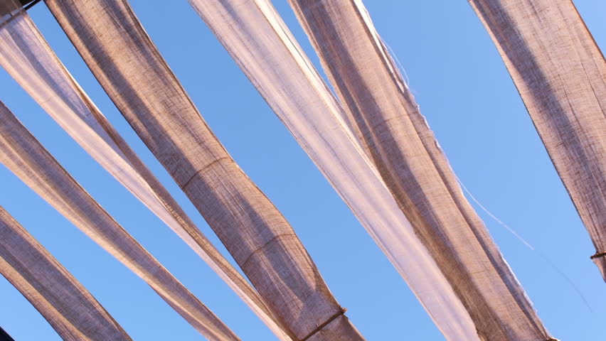 Fabric shades flowing in the wind with a clear blue sky backdrop, showcasing softness and motion