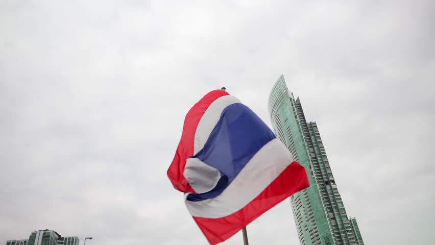 Close up of The national flag of Thailand waving in the wind on a cloudy day in Bangkok with skyscraper in the background 