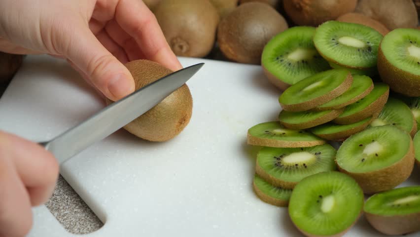The process of cutting fresh ripe kiwi into slices with a knife.