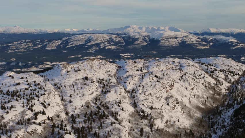 Soar over Fish Lake’s frozen expanse surrounded by snow-dusted mountains in Yukon. A tranquil aerial scene of Canada’s majestic winter beauty.