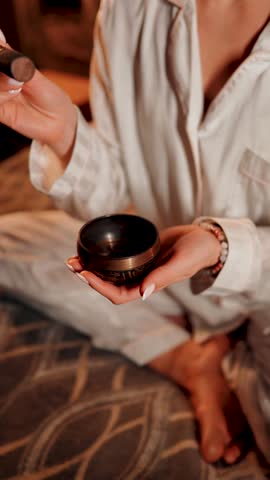 Woman uses Tibetan singing bowl for meditation in serene atmosphere at home