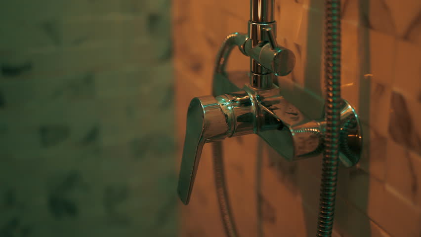 Hand is opening shower faucet. Guy turning water preparing to take shower in bathroom at home, close-up view. Daily routine, hygiene procedures, washing body concept. Dimmed lights in bath.
