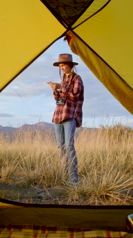 Girl photographer taking pictures with smartphone. joyful camper stands outside a cozy tent, fully appreciating the stunning beauty of nature in a remote setting
