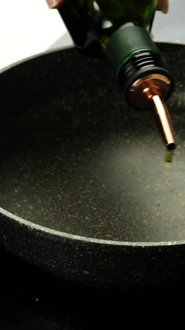 Hand pouring olive oil into a frying pan for cooking. preparing for frying a delicious dish in a cozy kitchen setting. The oil glistens in the pan