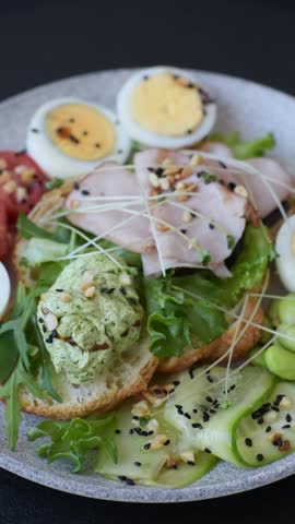 Healthy breakfast consisting of boiled eggs, slices of ham, tomatoes, green beans, aioli sauce on a dark concrete background