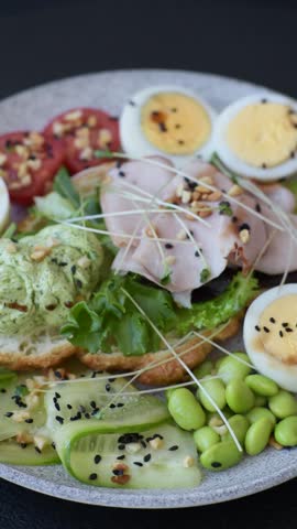 Healthy breakfast consisting of boiled eggs, slices of ham, tomatoes, green beans, aioli sauce on a dark concrete background