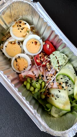 Healthy breakfast consisting of boiled eggs, slices of ham, tomatoes, green beans, aioli sauce on a dark concrete background