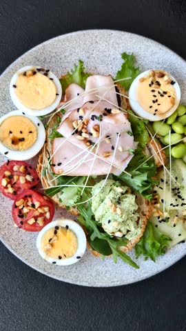 Healthy breakfast consisting of boiled eggs, slices of ham, tomatoes, green beans, aioli sauce on a dark concrete background