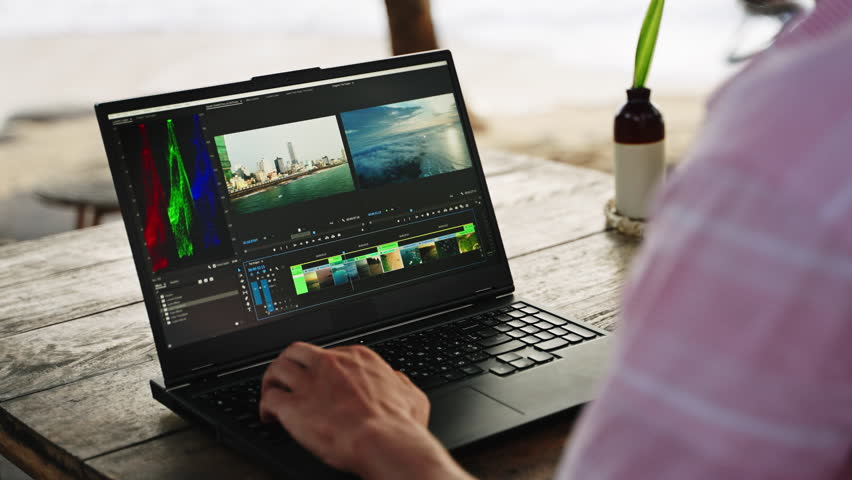 Video editor works on laptop, color grading clips at beach cafe. Sunset over sea, professional edits travel footage near ocean. Creative digital nomad, remote tech job lifestyle by water. Slow motion.