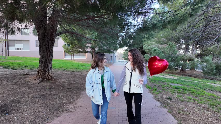 Lesbian couple walking in park with heart balloon on valentine
