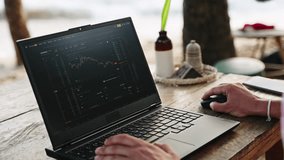 Crypto trader analyzes market graphs on laptop at beachside cafe. Sunset, mouse clicking, analyzing patterns, freelance finance work. Relaxed setting merges trading with leisure time at ocean shore. - Powered by Shutterstock - Get 15% off with code: PIKWIZARD15