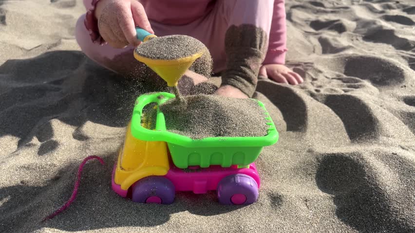 Cute baby girl playing with toy car and shovel on yellow sand on the beach by the sea