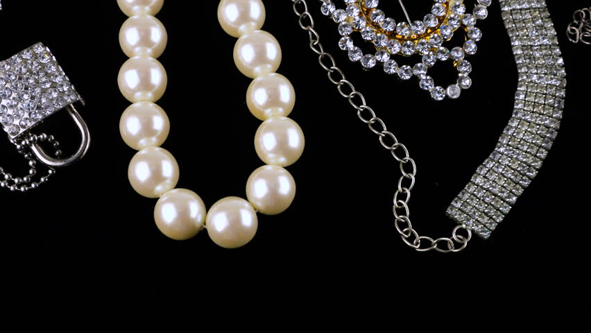 Vintage costume jewelry, brooches and necklaces, with crystals and imitation pearls on a rotating black velvet display case.