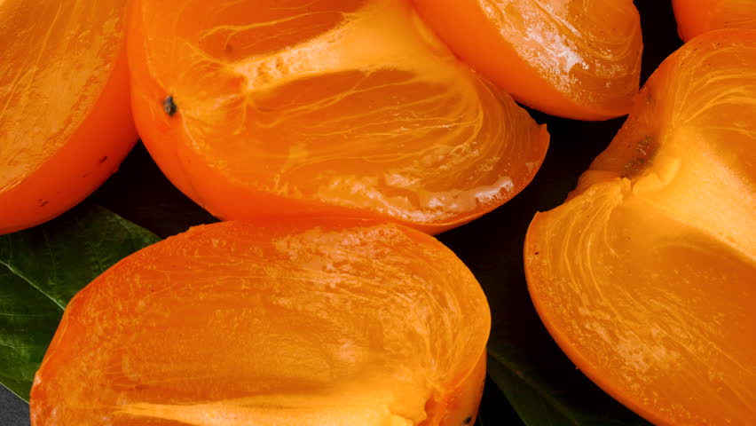 Fresh ripe persimmon slices rotate on a stone board.