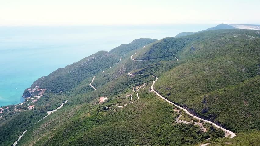 Aerial view of winding roads and lush green hillsides in Parque Natural da Arrábida, Portugal. The stunning coastal scenery offers a picturesque blend of natural beauty and serene landscapes