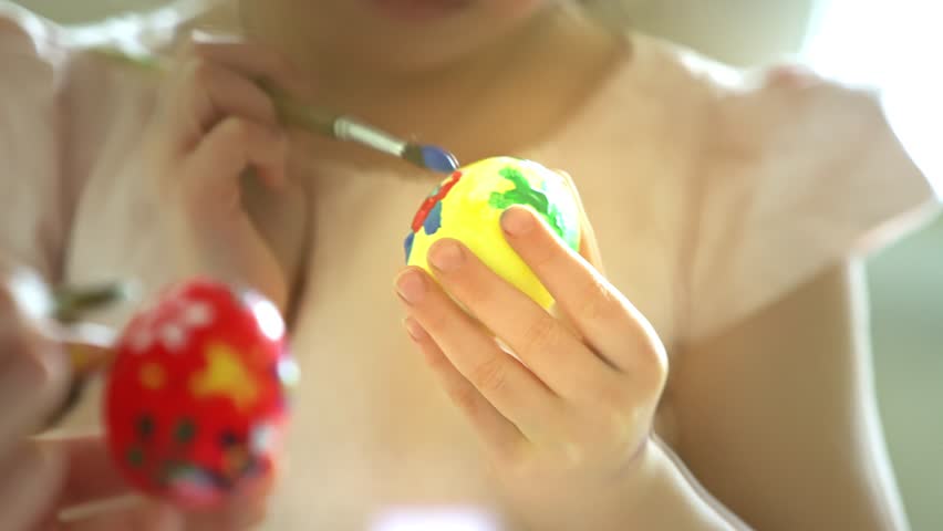 Mother and daughter painting Easter eggs together at home. Bright festive decorations, joyful atmosphere, creativity, and bonding. Colorful paints, bunny ears, and spring mood.