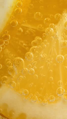 Camera movement on carbonated drink with fresh lemon slices and ice. Macro bubbles in glass with mineral water. Soda water. Lemonade. Vertical shot