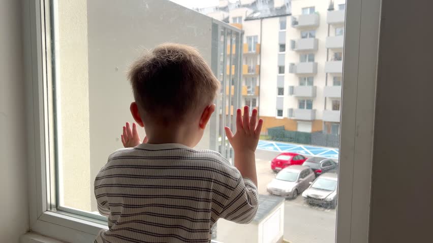 A small child sits down and looks out the window at the street