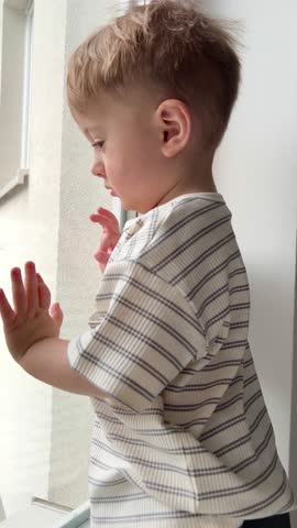 A small child sits down and looks out the window at the street