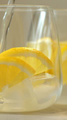 Carbonated drink is poured into glass with fresh lemon slices and ice. Mineral water. Soda water. Lemonade. Vertical shot