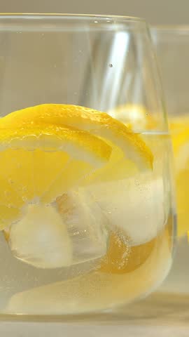 Carbonated drink is poured into glass with fresh lemon slices and ice. Mineral water. Soda water. Lemonade. Vertical shot