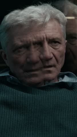 Vertical low key shot of elderly Caucasian man with grey hair rubbing his face feeling anxious and disoriented staying alone at home in dark living room