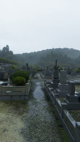 A serene Japanese cemetery with stone graves, trees, and misty hills at Osaka-Katsuoji