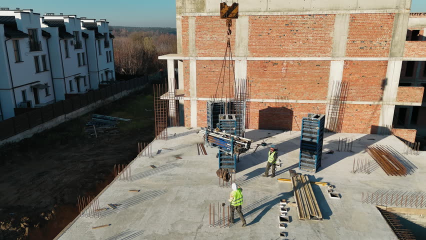 Aerial view Construction worker directing crane on building site, A construction worker wearing a safety vest and helmet directs a crane lifting materials
