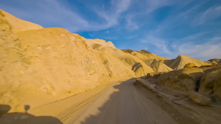 Capture the breathtaking view of Twenty Mule Team Canyon Road during sunset in Death Valley National Park, California, where the sunlight illuminates the mountains.