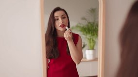 An elegant woman in a red dress is applying red lipstick looking at her reflection in a bedroom mirror before a night out. - Powered by Shutterstock - Get 15% off with code: PIKWIZARD15