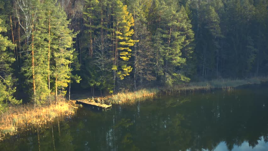 Forest lake footbridge, deep woods, blue water, sunrise, golden hour, aerial drone video