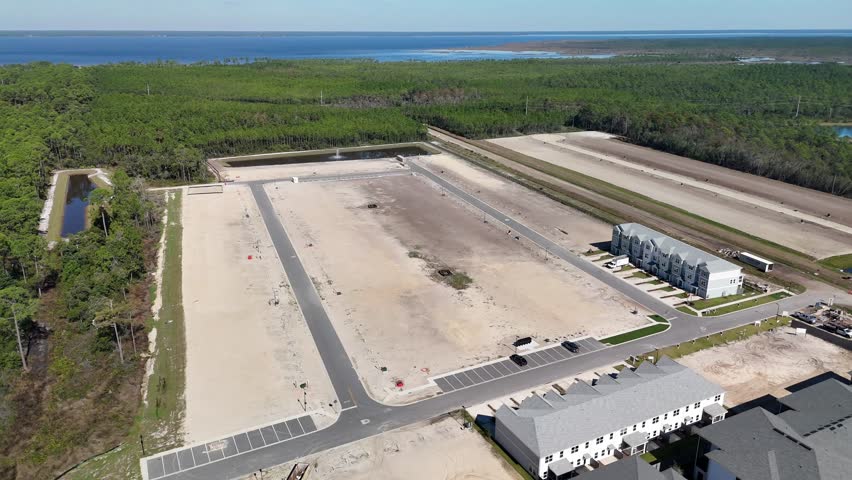 An Aerial View of Cleared Land Plots, Retention Ponds, and Residential Buildings Surrounded by Dense Greenery and Water in Panama City, Florida