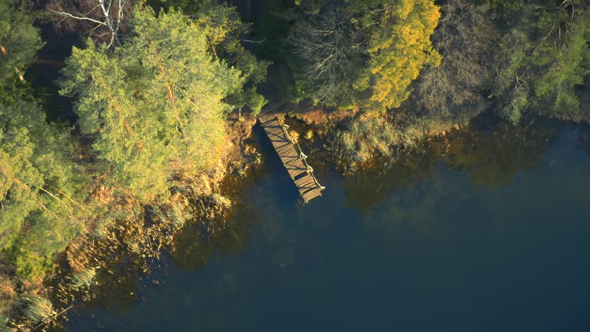 Forest lake footbridge, deep woods, blue water, sunrise, golden hour, aerial drone video