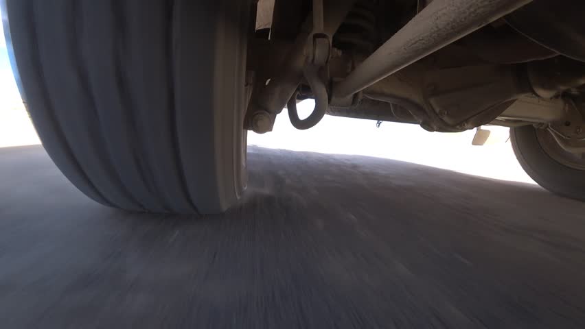 The camera is fixed on the bottom of the car, a view of the wheel and suspension while driving. Off-road, rocks and dust. The suspension works well off-road and bumps. Deserted area. Tire deformation
