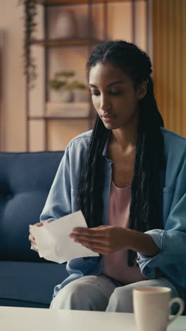 Young African American woman reads a bad news letter, feeling deeply discouraged