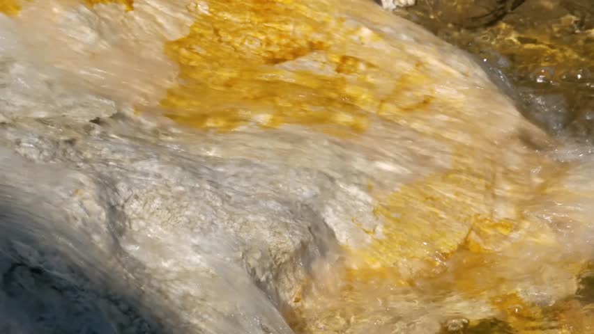 Water running over stones with sulphur runoff, yellowstone national park, wyoming, USA.